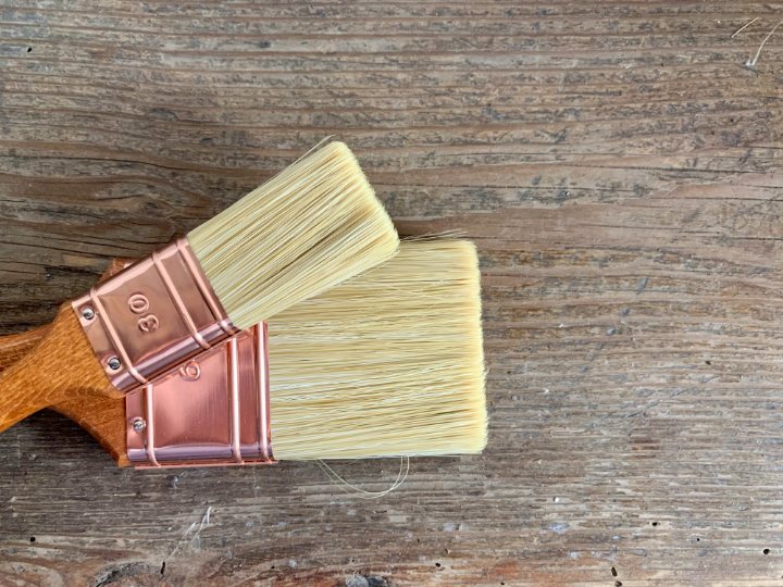Two clean brushes with copper ferrules, laid on a weathered wooden board