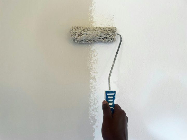 A roller laying a pale first coat on a wall, the pass still wet